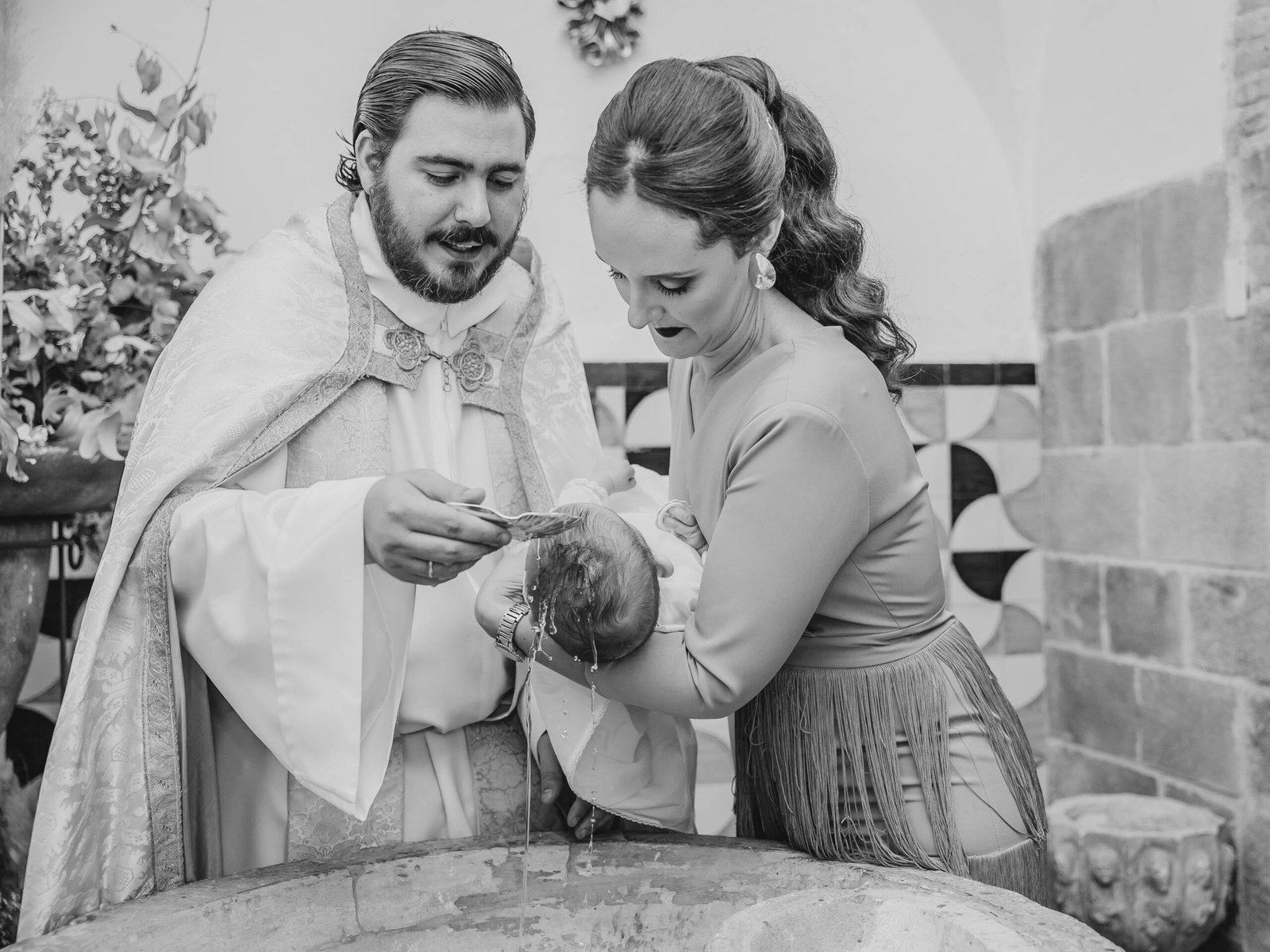 Momento del bautismo: el sacerdote vierte agua sobre el bebé sostenido en brazos, fotografía en blanco y negro de Garoy